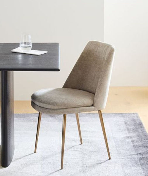 1. Modern West Elm dining chair with taupe upholstery and gold legs, beside a dark table on a light rug.