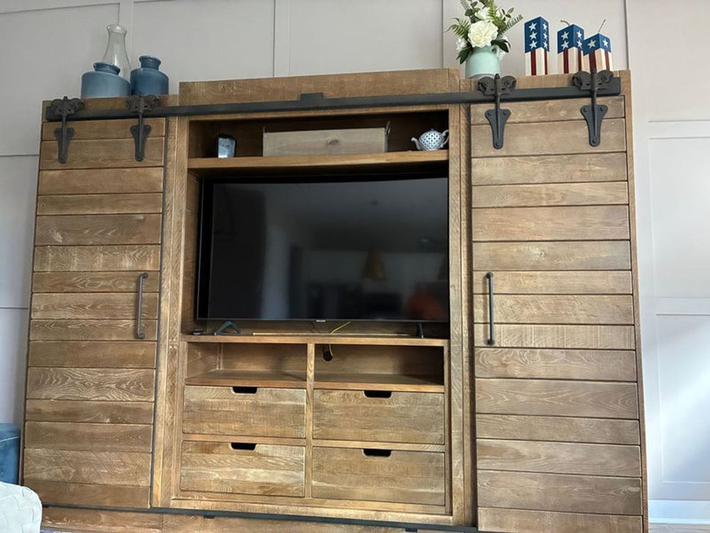 1. Arhaus wooden entertainment center with sliding barn doors, drawers, and TV displayed at the center.
