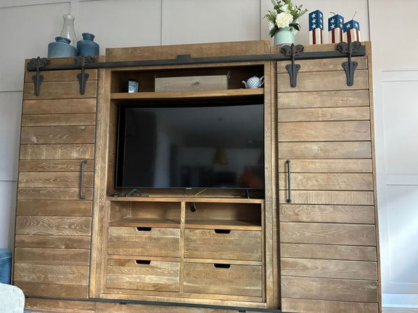 1. Arhaus wooden entertainment center with sliding barn doors, drawers, and TV displayed at the center.