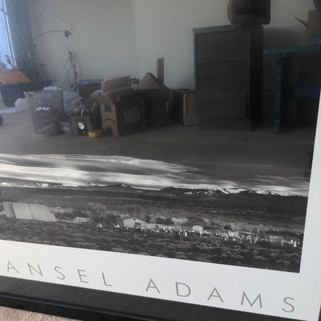1. Framed Ansel Adams black and white print reflected in a room with boxes and furniture, emphasizing the photograph.