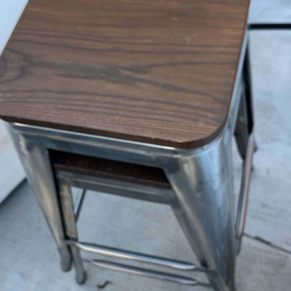 1. Close-up of a metal stool with a dark wooden seat, showing its sturdy industrial design.
