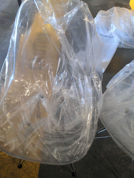 1. Clear plastic dining chair with metal legs, partially wrapped in protective plastic, on a concrete floor.