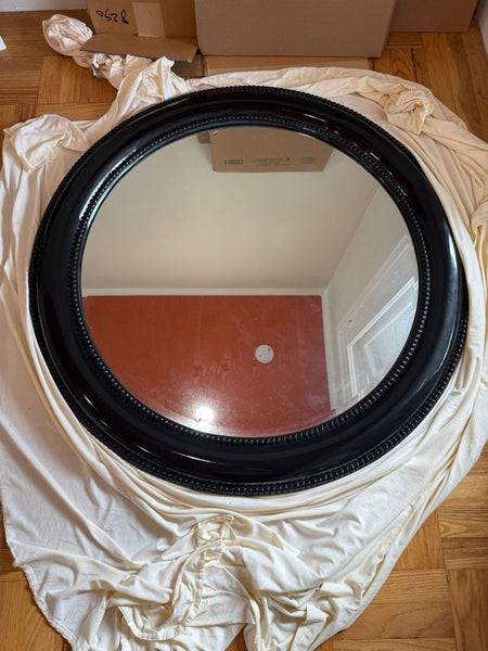 1. Round Howard Elliott mirror with a glossy black beaded frame, displayed on white fabric and parquet flooring.