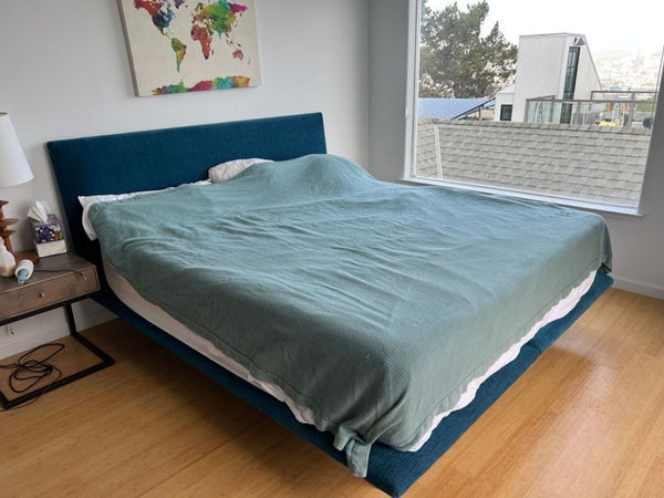 1. Room & Board bed frame with blue upholstered headboard in a modern bedroom with large window.