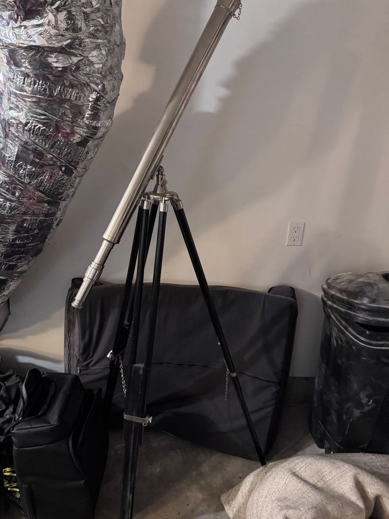 1. A metal telescope mounted on a black tripod, standing in a garage with miscellaneous items around it.