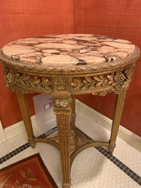 1. Ornate round side table with a pink and brown marble top, gold carved details, and fluted legs, set in a corner.  