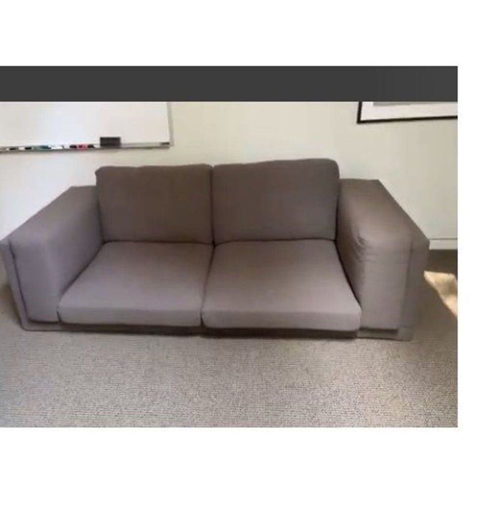Used Ikea 3-seat sofa with wide armrests and muted gray upholstery, placed in an office setting.