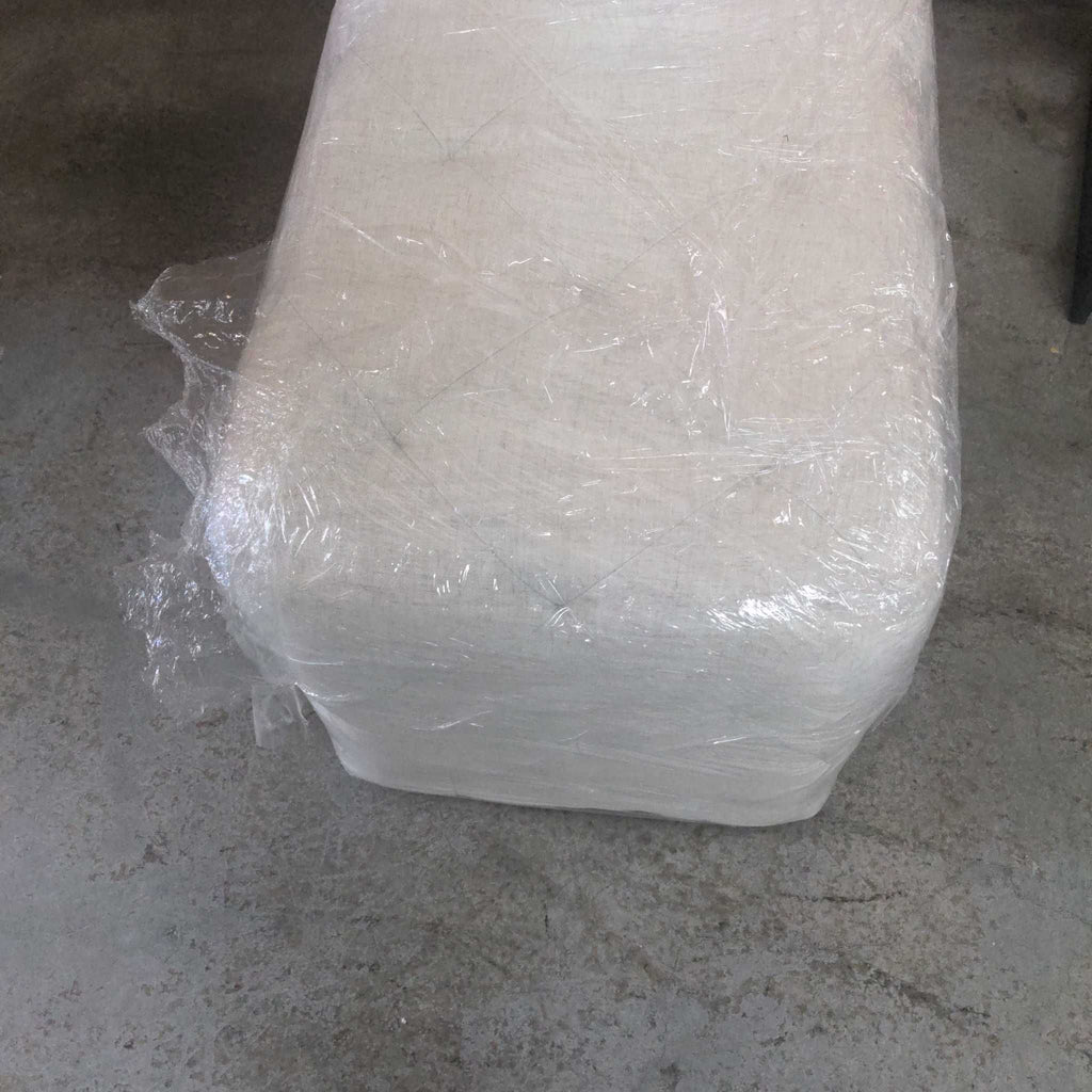 2. Top view of a Target brand white ottoman, partially wrapped in clear plastic, placed on a cement surface.