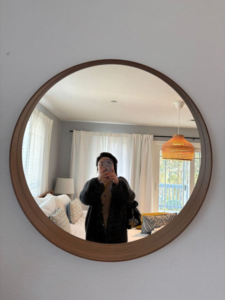 1. Round Ikea mirror with wooden frame, reflecting a cozy bedroom with white curtains and a rattan lamp.