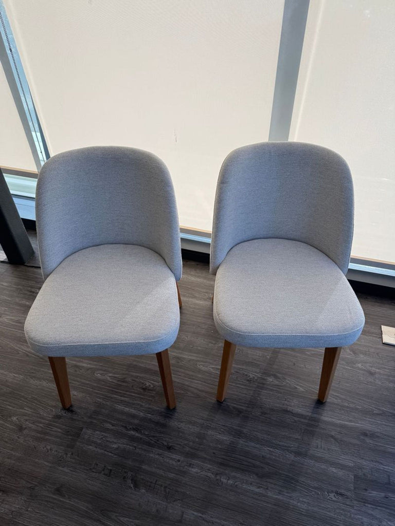 1. Pair of modern Article dining chairs with light grey upholstery and wooden legs on dark flooring.