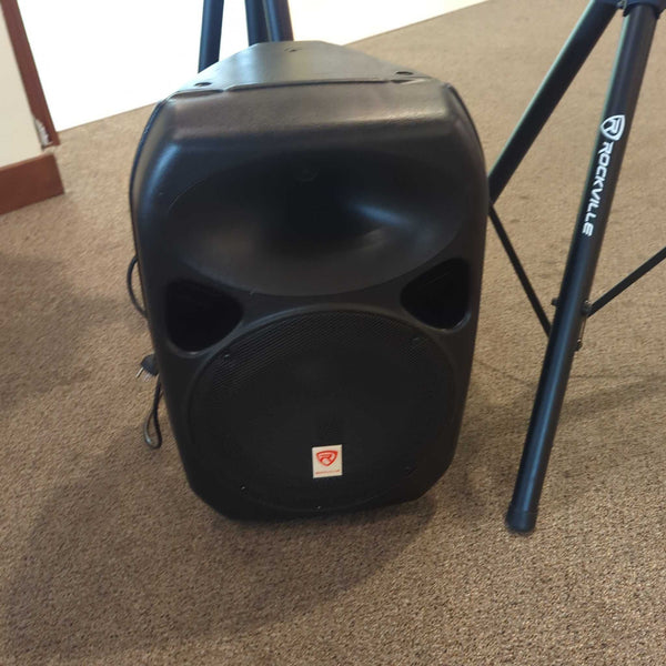 1. Rockville black audio speaker on carpet, positioned near a labeled tripod stand, for audio equipment use.