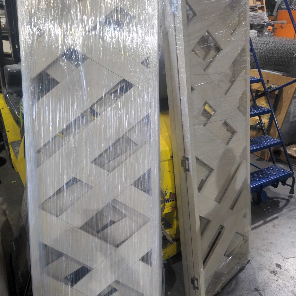 1. Two white wooden room dividers with crisscross patterns are wrapped in plastic in a warehouse setting.