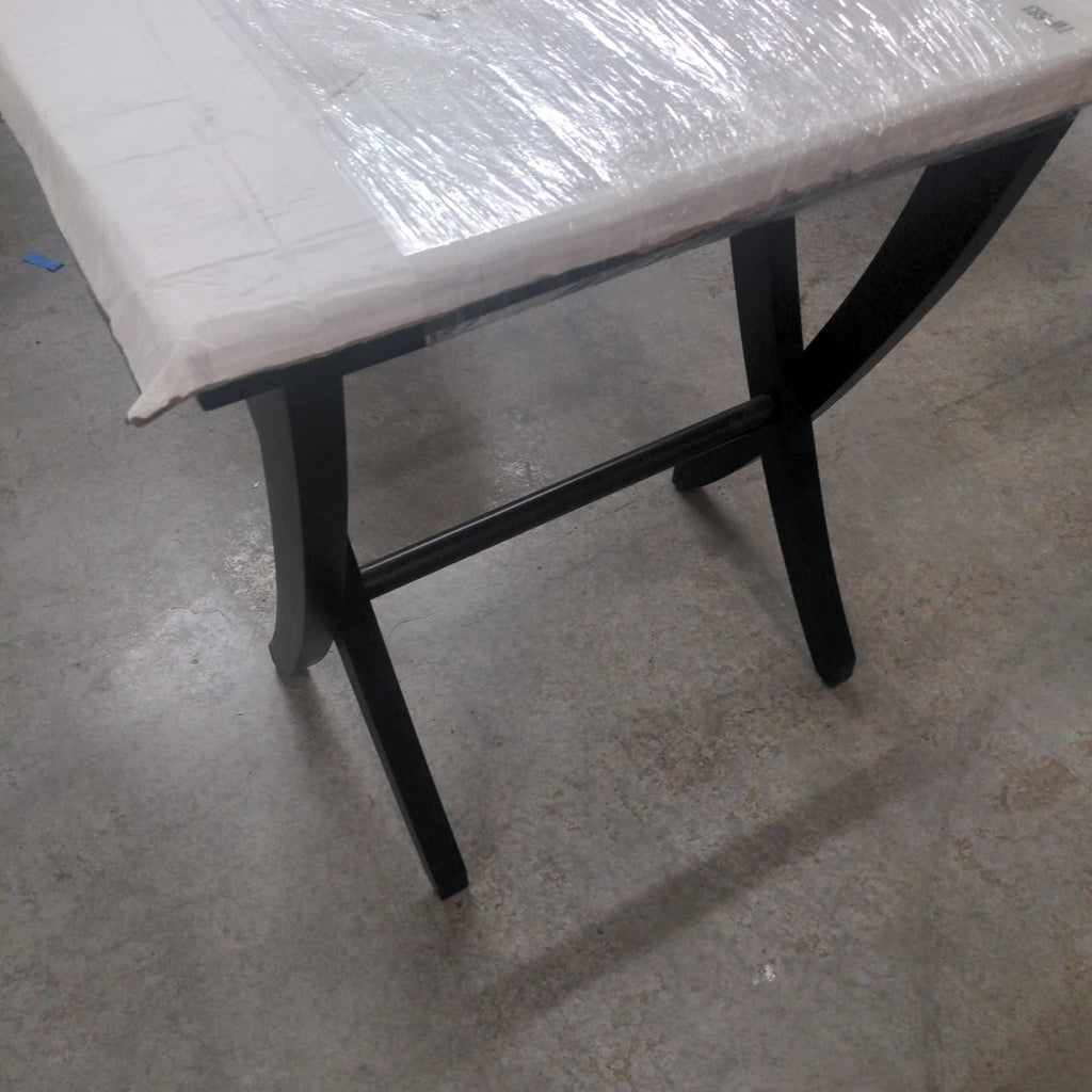 1. Black side table with curved legs and a rectangular top, partially wrapped in protective plastic, on concrete floor.