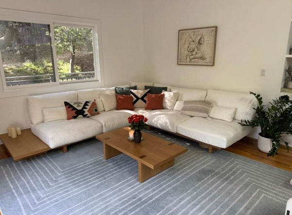 White Castlery sectional sofa wrapped for moving, showing modern design and low-profile wooden legs.