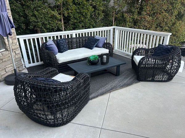 Wicker outdoor set with sofa, two chairs, table, and cushions, ideal for patio or garden relaxation.