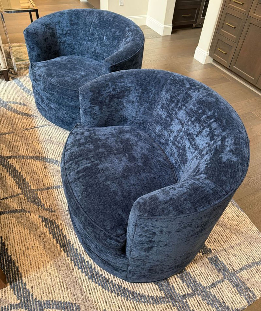 Two round, modern lounge chairs upholstered in textured blue fabric, placed on a patterned area rug.