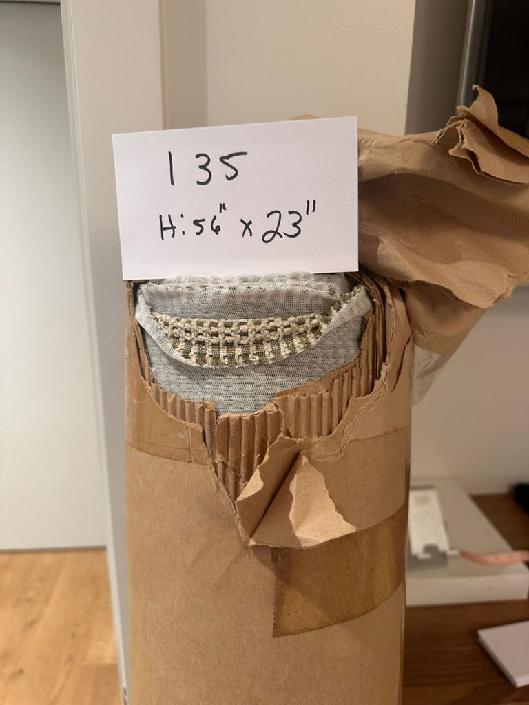 2. Close-up view of a cardboard tube with torn edges, showing rolled grey fabric and a handwritten size note.  