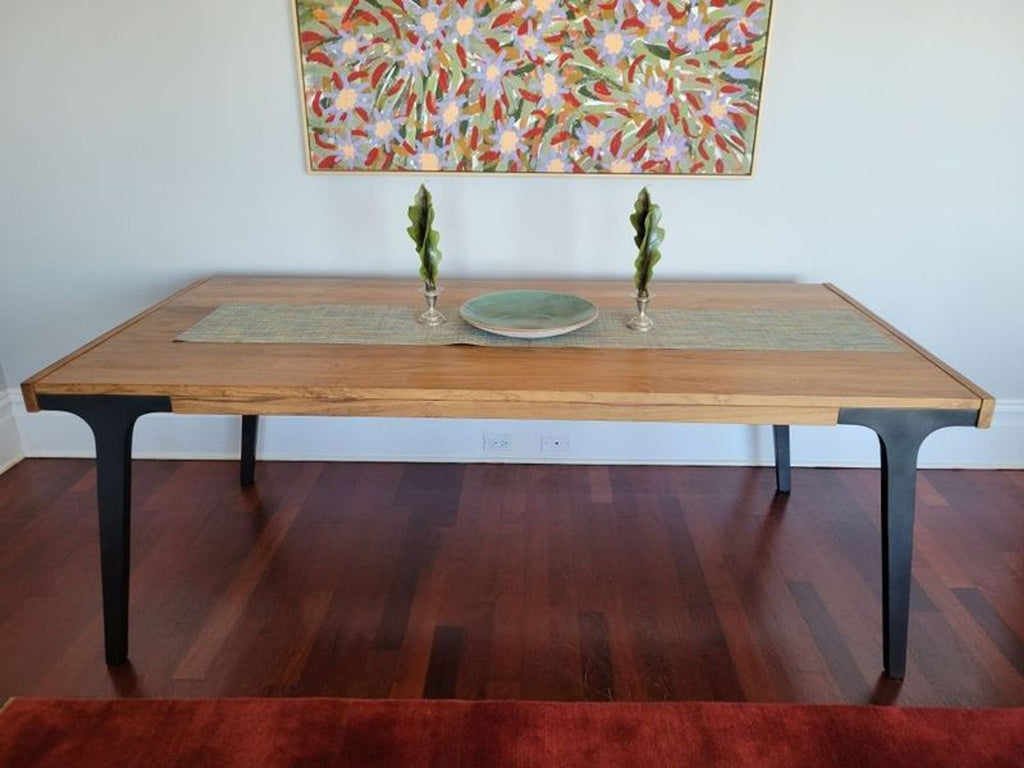 3. Crate & Barrel wooden dining table with black legs, styled with a runner, vase, and plate beneath wall art.