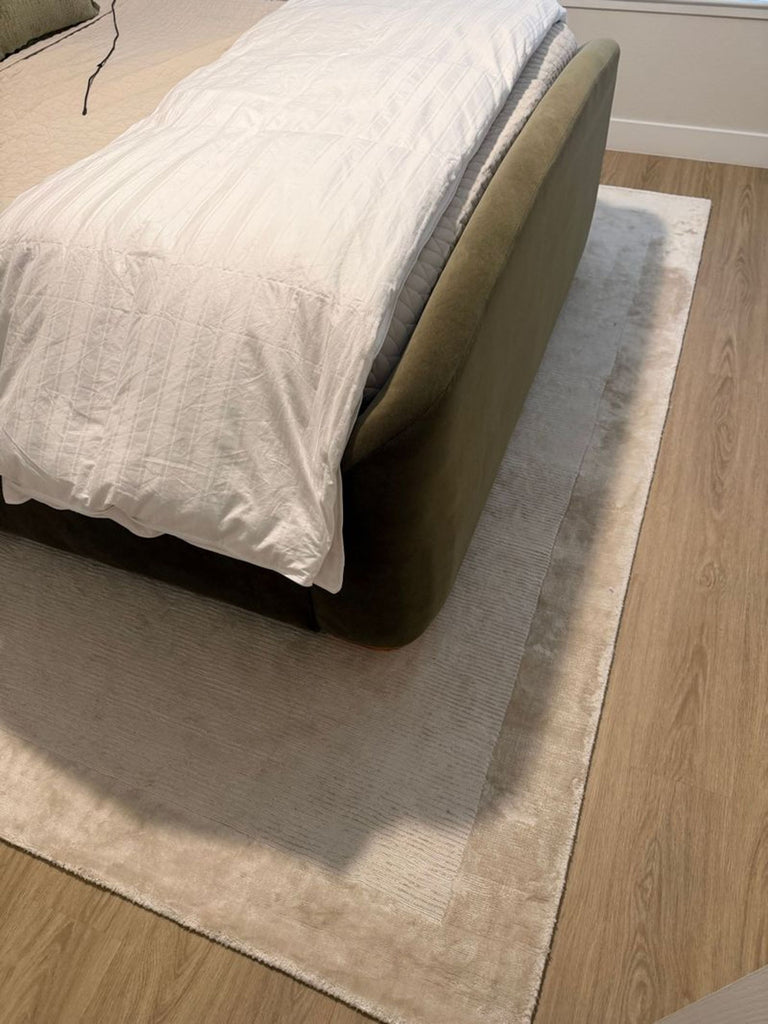 1. West Elm beige area rug under a modern bed, placed on a light wood floor in a bedroom.  
