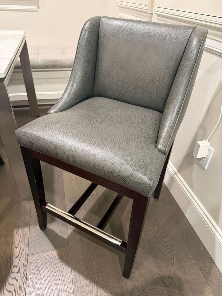 1. Gray upholstered bar stool with wooden legs and metal footrest, placed next to a dining table in a modern room.