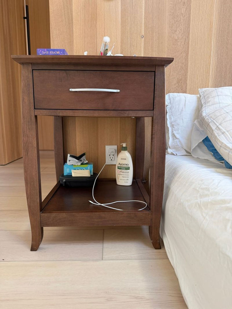 3. Reperch end table beside a bed, featuring drawer, shelf, and assorted personal items placed on top and below.