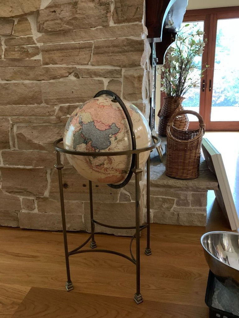 Decorative globe on a stand next to a stone wall with basket decor.