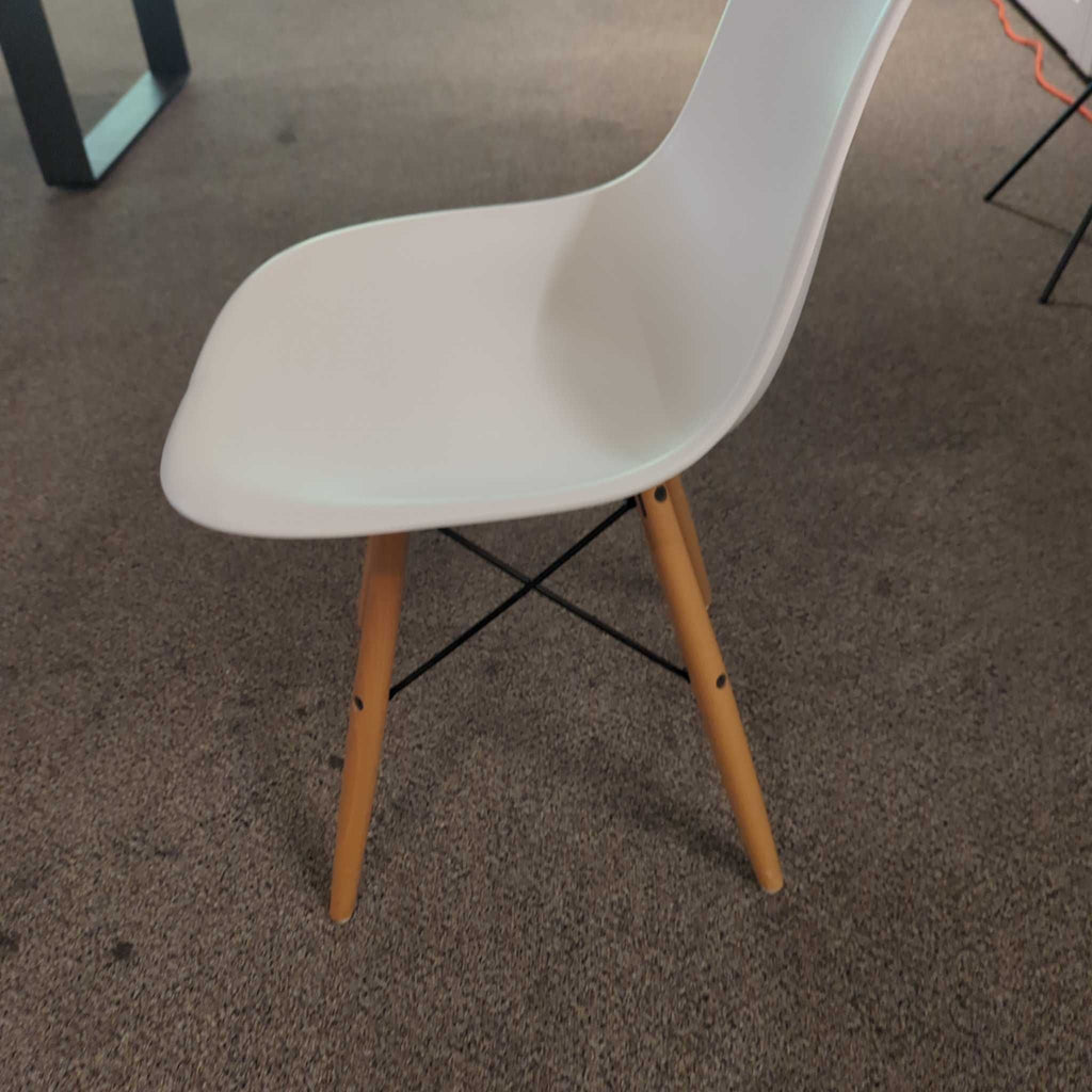 Side view of a white dining chair with wooden legs and black metal supports on carpeted flooring.