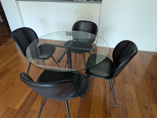 1. Room and Board dining set featuring a round glass table and four black chairs on a wooden floor.
