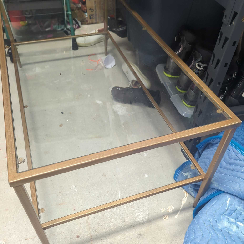 2. Glass coffee table featuring a gold metal frame, pictured in a garage with various items around it.