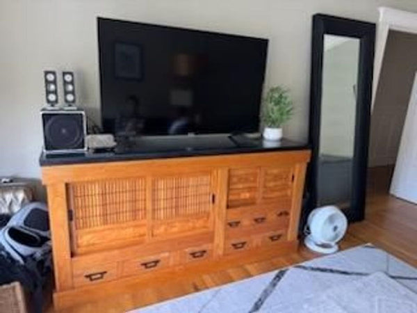 1. Wooden entertainment center with sliding doors, drawers, and a black top, supporting a large flat-screen TV.