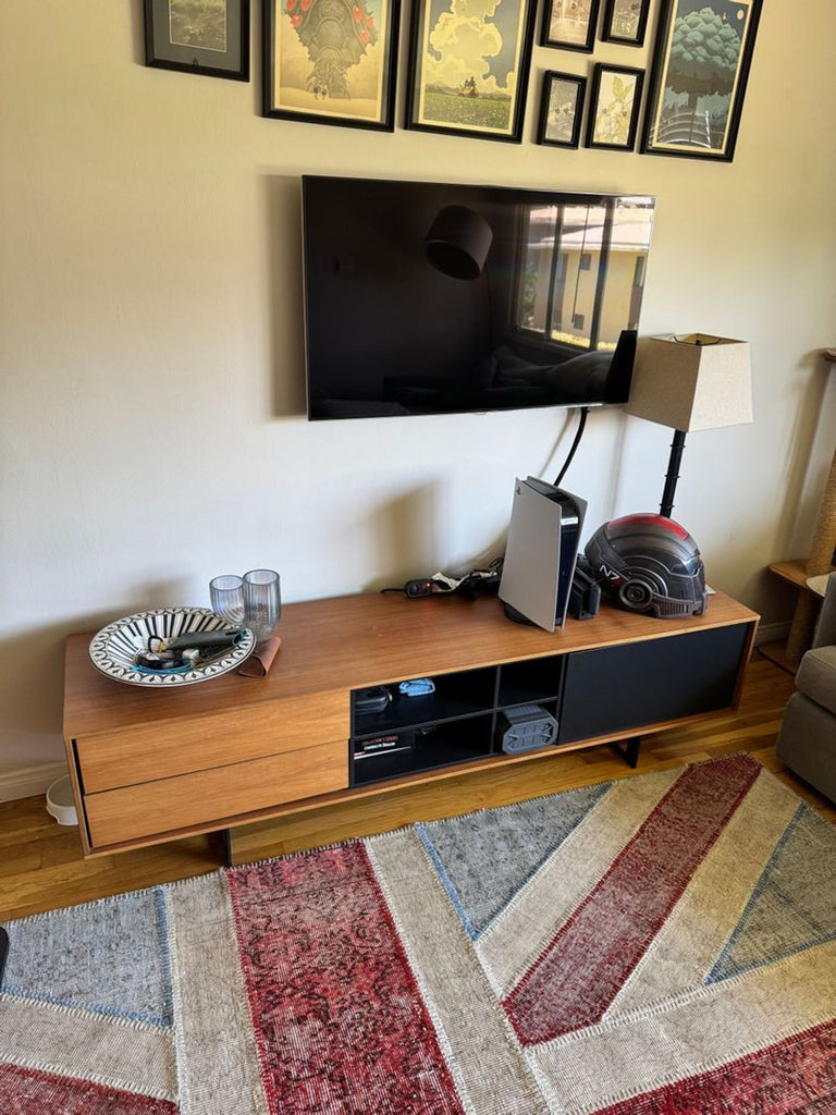 Sleek wooden media unit with black accents. TV, decor, and lamps on top, rug underneath.