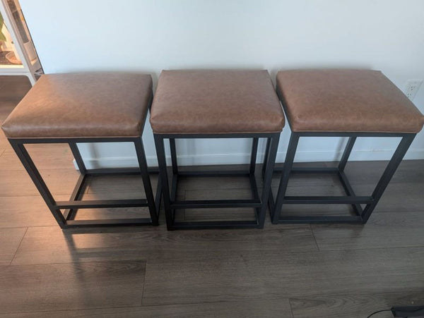 Set of three Reperch stools with brown cushioned seats and black metal frames lined up on wood flooring.