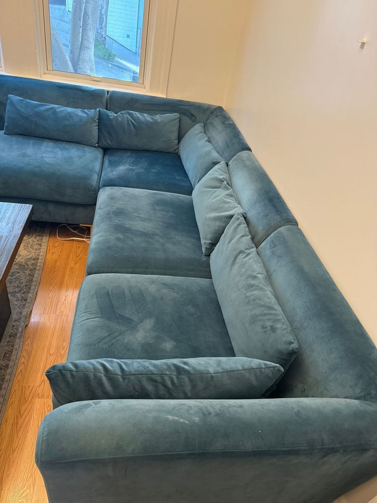 1. Blue velvet sectional sofa in an L-shape, placed in a corner by windows on hardwood flooring.