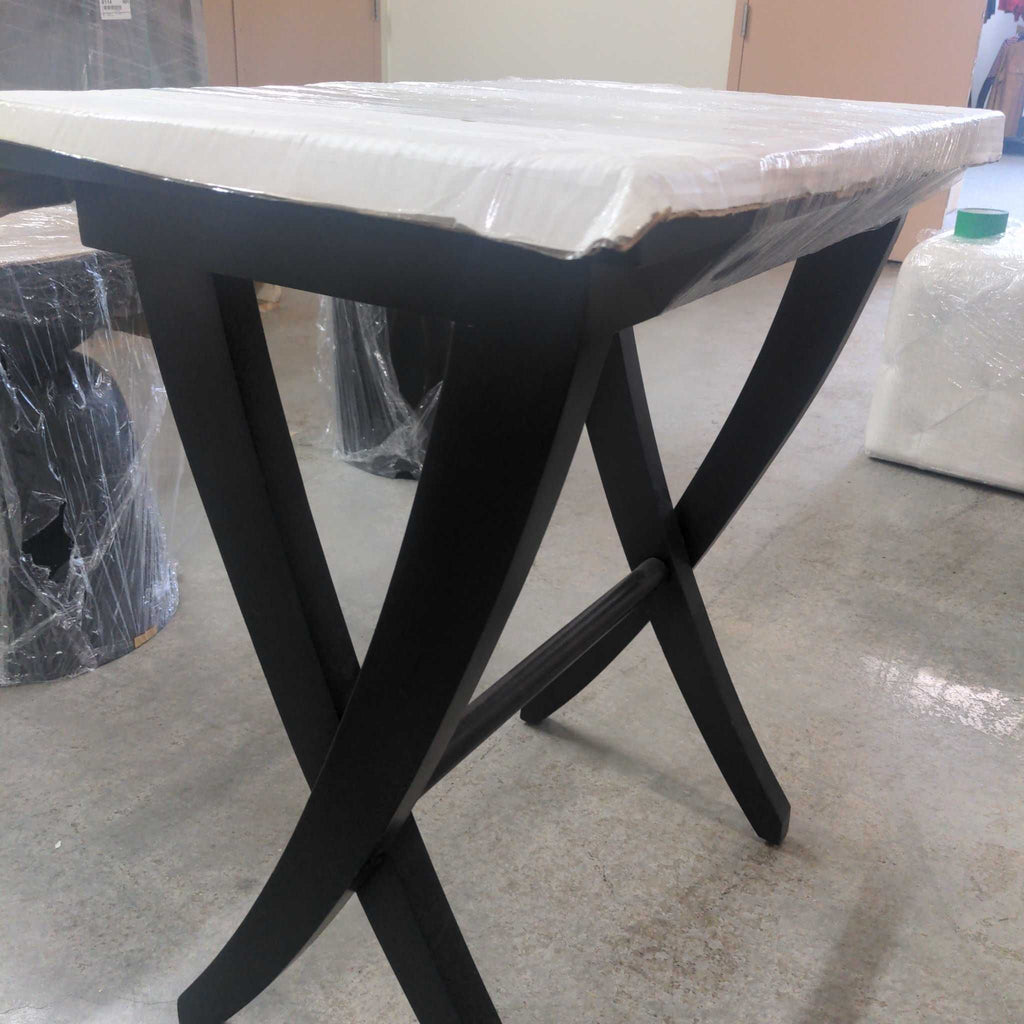 2. Angled view of a black console table, curved legs, wrapped top, placed in a warehouse setting.