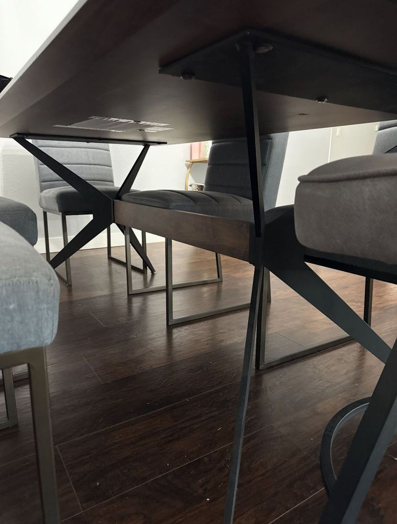 Underside view of a custom dining table, highlighting black metal cross-braced legs and sleek gray chairs.