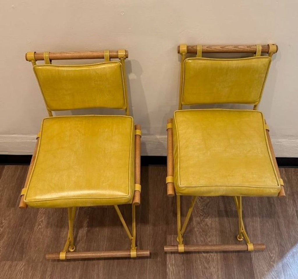 Top view of two yellow Design Frères stools with soft leather seats, wooden details, and sturdy metal frames.
