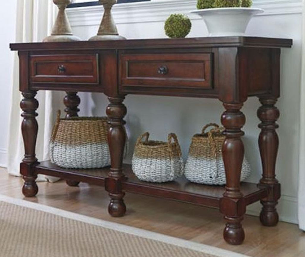 1. Dark wood side table with carved legs, two drawers, and woven baskets on the lower shelf in a living room.