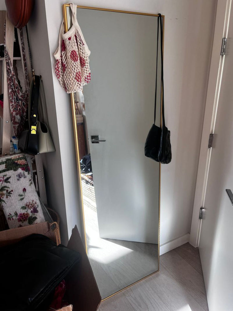 1. Rectangular Pottery Barn mirror with gold frame, leaning against wall, bags hanging on corner, in a hallway.