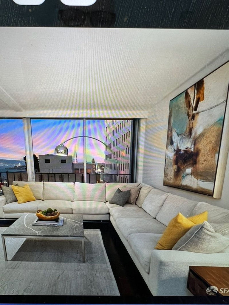 3. A. Rudin sectional sofa in a bright room, with yellow accent pillows, abstract art, coffee table, and cityscape views.