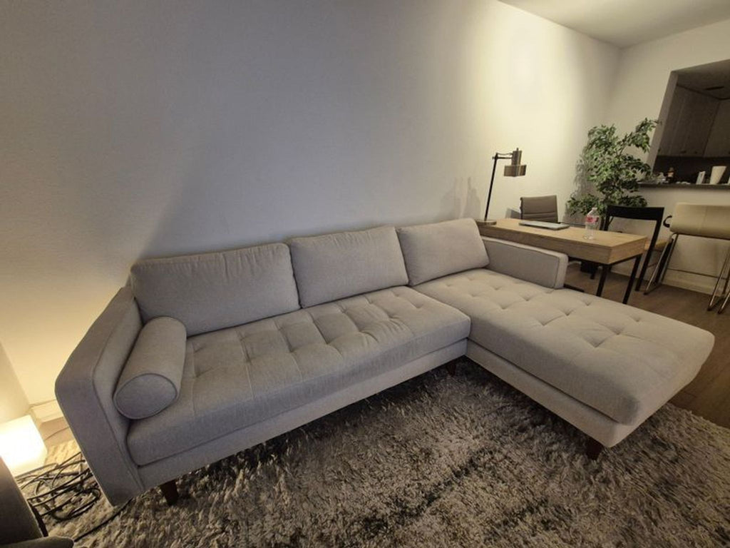 1. Light gray LUKAS OPTICAL sectional sofa with tufted cushions and bolster pillow on a shaggy rug in living room.