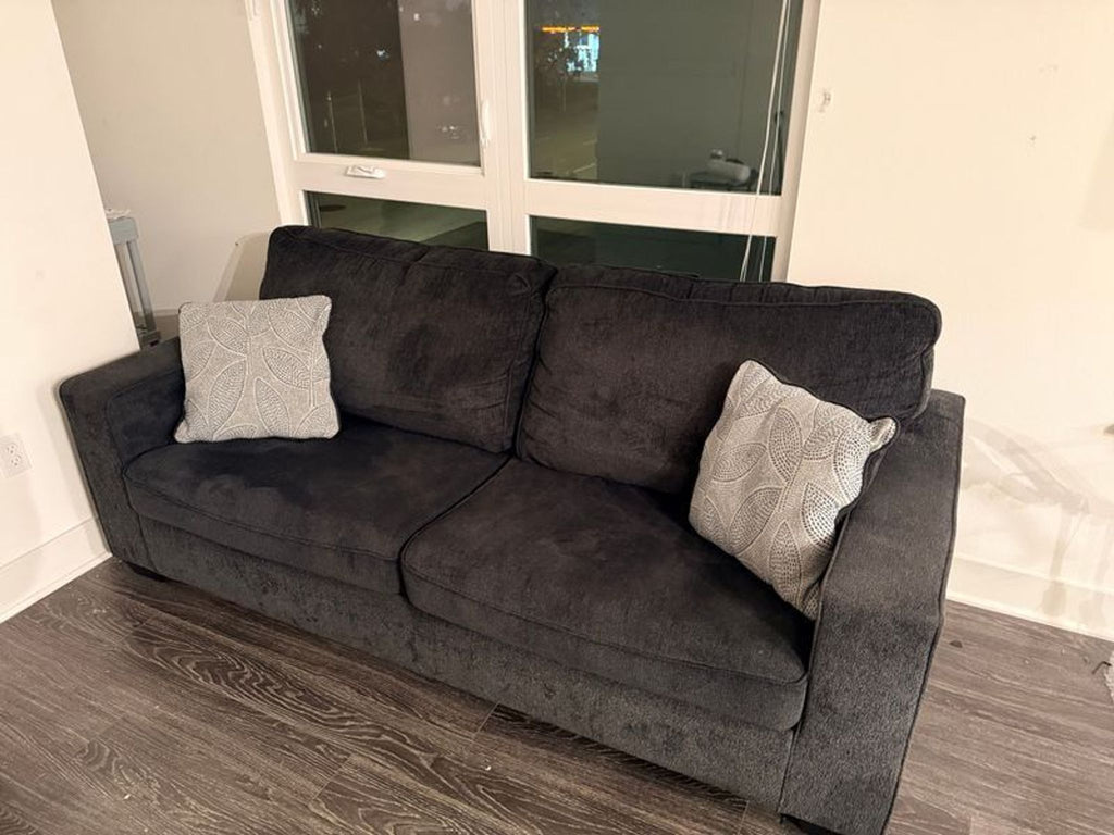 1. Dark gray Ashley Furniture sleeper sofa with two patterned cushions, set in a modern room by a window.