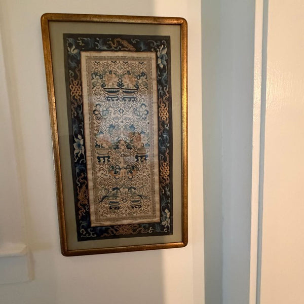 1. Framed textile art with intricate blue, gold, and cream patterns, displayed on a wall.