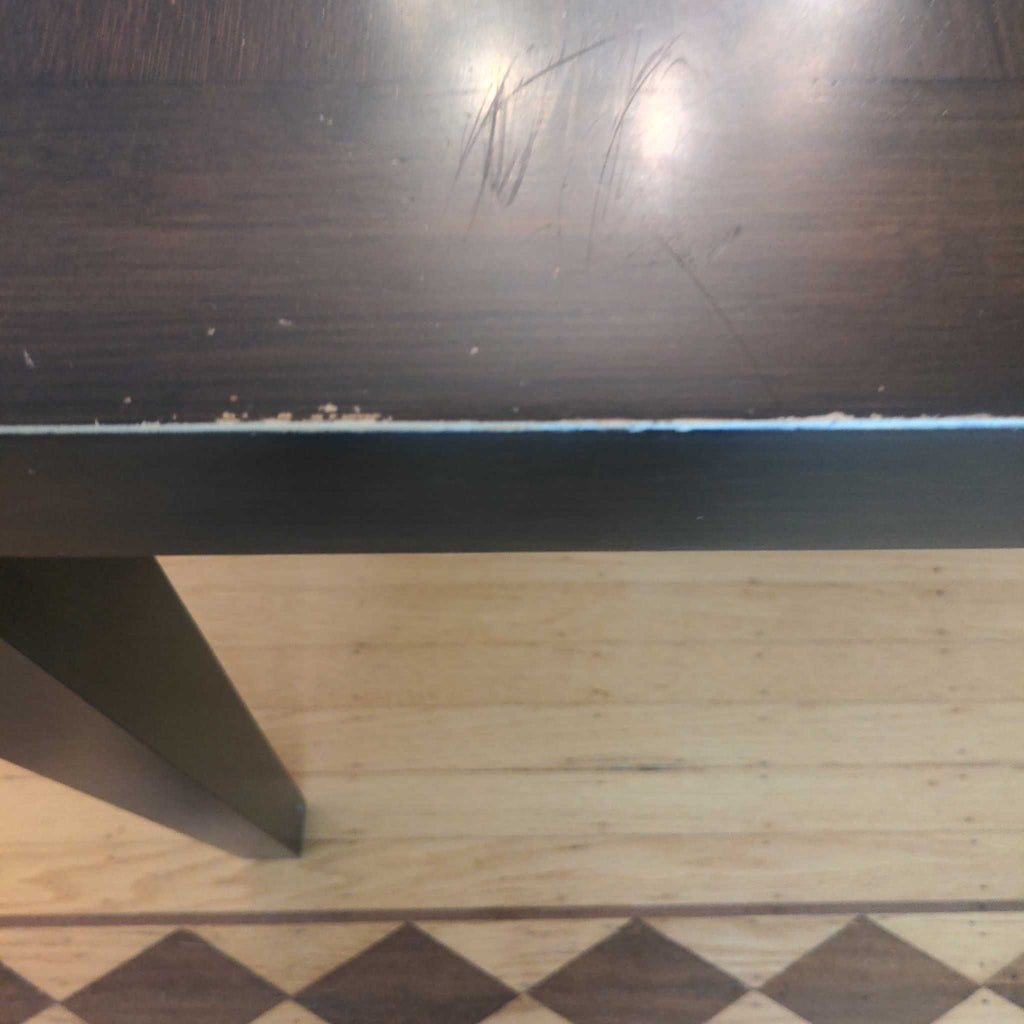 1. Close-up of a Room and Board dining table showing edge wear and surface scratches on the dark wood finish.