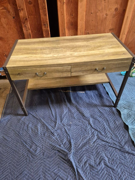 1. Rustic wooden desk with black metal frame, two central drawers, and lower shelf, placed on a blue quilted blanket.