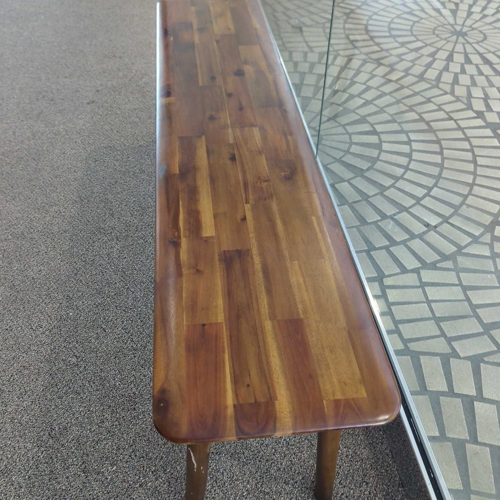 1. Long wooden EQ3 bench with a smooth, polished finish, placed beside a glass wall on carpeted flooring.