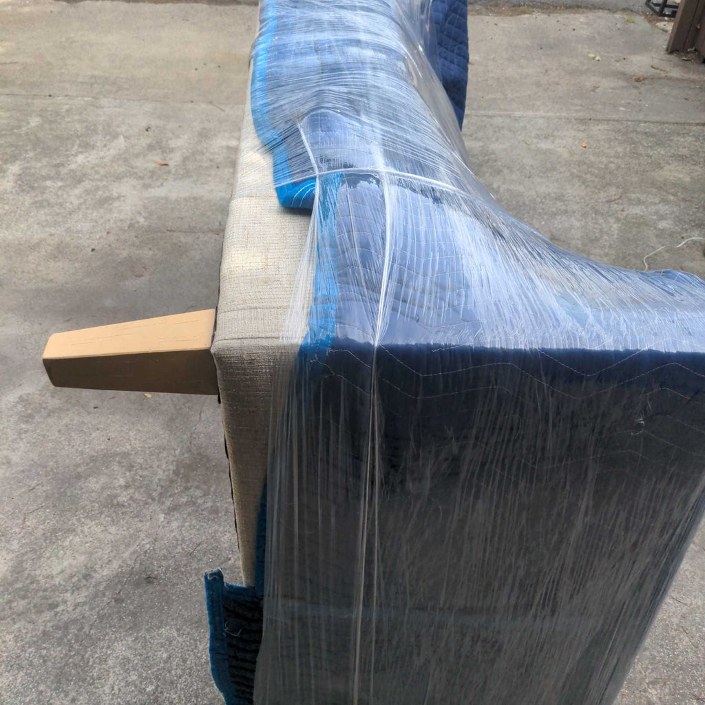 2. Side view of a Reperch 3-seat sofa, partially wrapped in blue padding and clear plastic for protection.