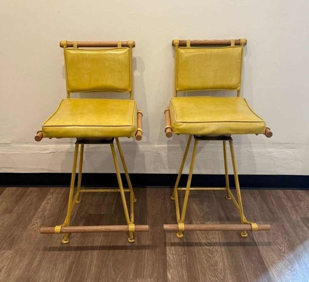 Pair of Design Frères stools with yellow metal frames, yellow leather cushions, and wooden accents, side by side.  