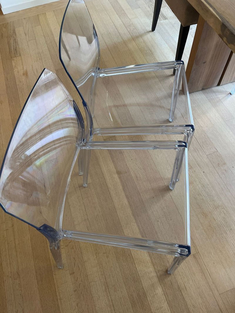 1. Two clear acrylic CB2 dining chairs with modern design placed side by side on a wooden floor.