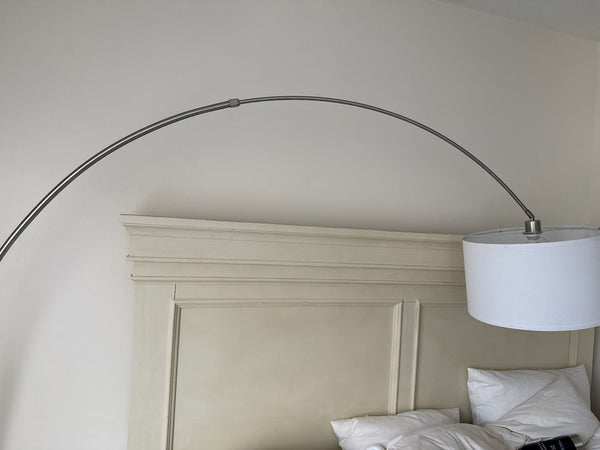 1. Arc floor lamp with a white drum shade, positioned beside a beige headboard and white pillows.