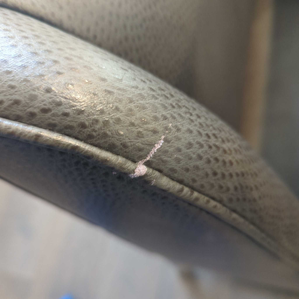 2. Close-up of a small scratch and abrasion on the textured gray upholstery of the stool's armrest.